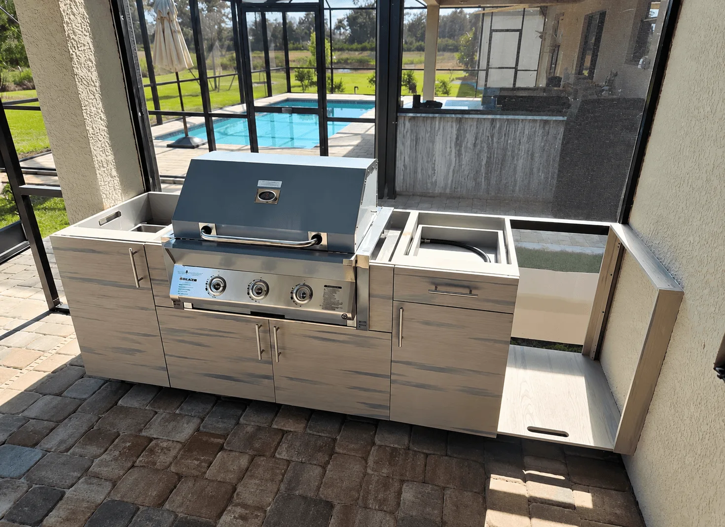 Outdoor kitchen island with built-in stainless grill and weathered wood cabinets on a screened patio