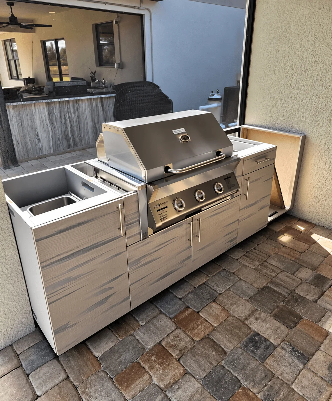 Outdoor kitchen island with stainless sink insert and matching cabinets under a covered patio